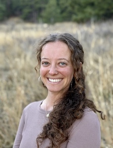 Headshot picture of clinician Alana in a grassy field. She is smiling and has a purple shirt and long brown curly hair.